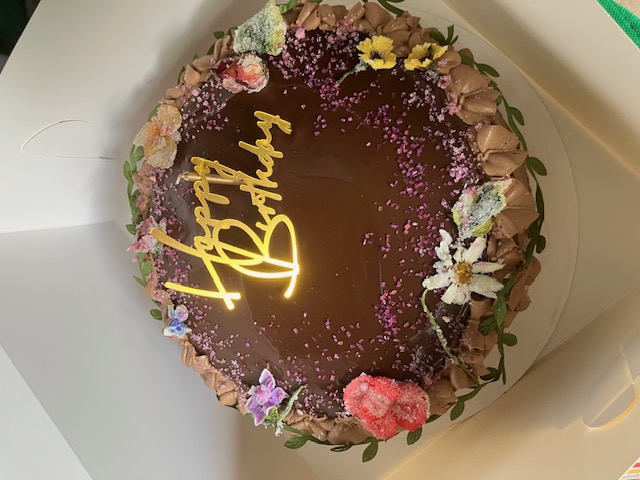 Chocolate birthday cake decorated with flowers and a gold birthday topper