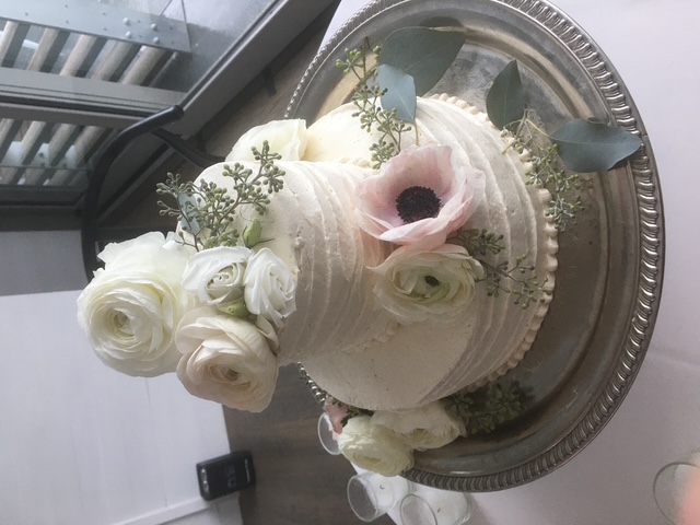 Two-tier ivory wedding cake with white roses and a pale pink flower